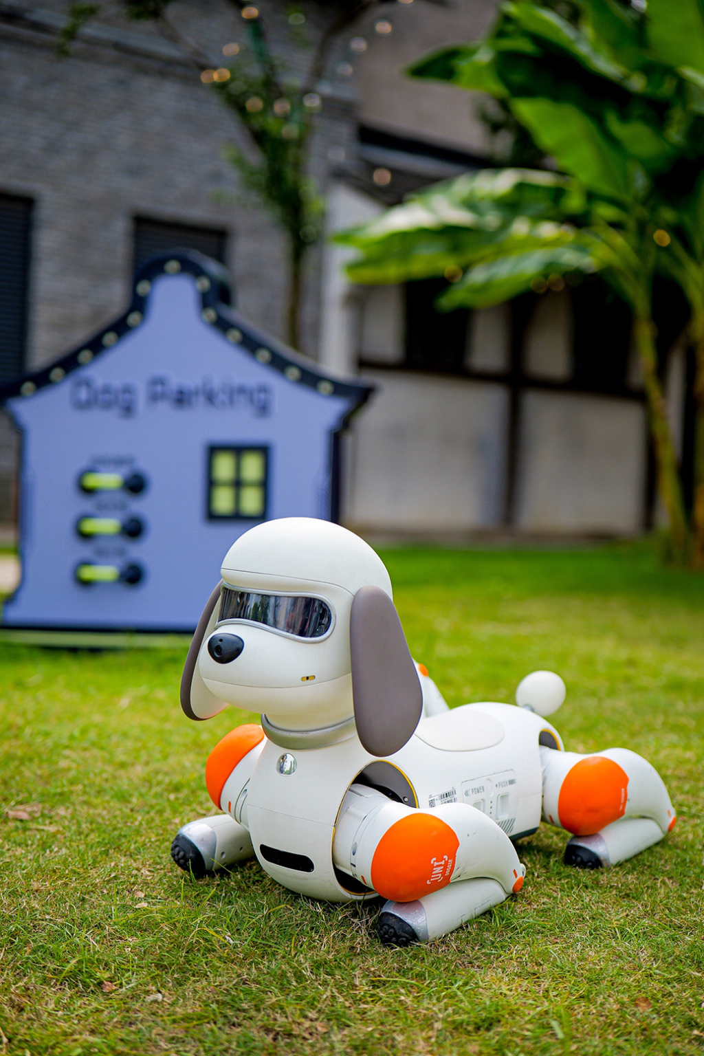UNI-DOGGIE机器狗趴卧在草坪上，旁边是Dog Parking创意标识牌